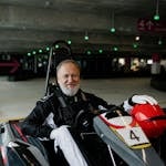 Elderly man in a go-kart smiles while racing indoors. Perfect for senior sports themes.