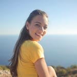 Young woman in a yellow shirt smiles by the sea, enjoying the outdoor view.