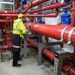 Engineer with safety gear inspecting red industrial piping system indoors.